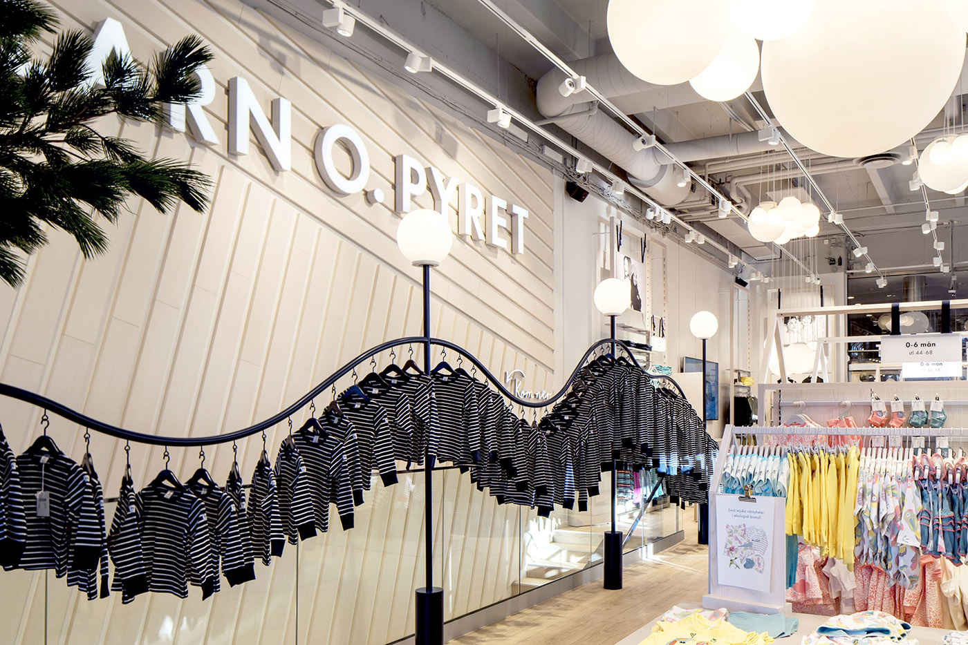 Butikskoncept för varumärket Polarn och Pyret. Randiga blå tröjor i en böljande upphängning samt färgglada kläder i bild